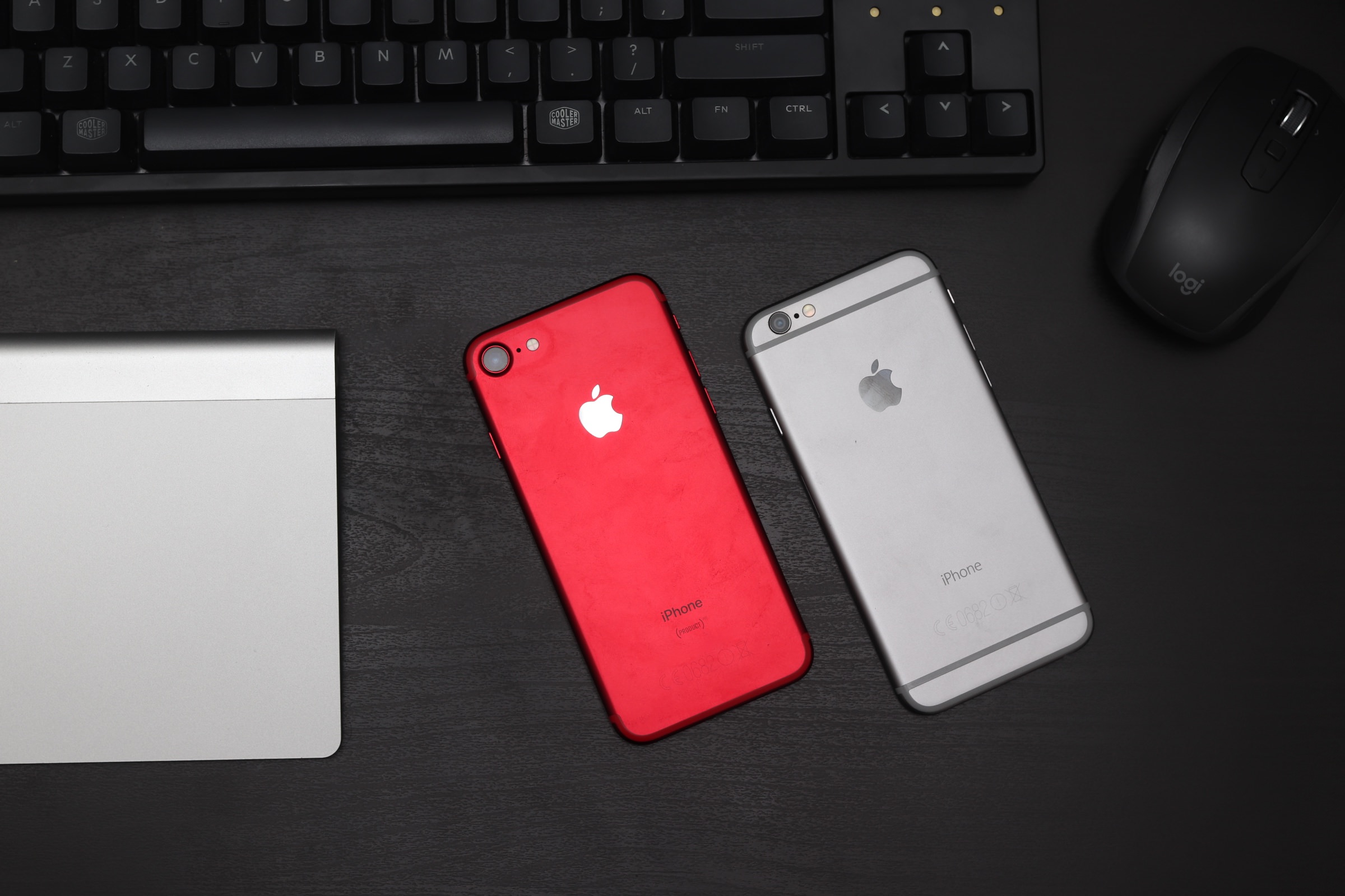 Two iPhones facing down on a desk, surrounded by computer peripherals like keyboard and mouse.