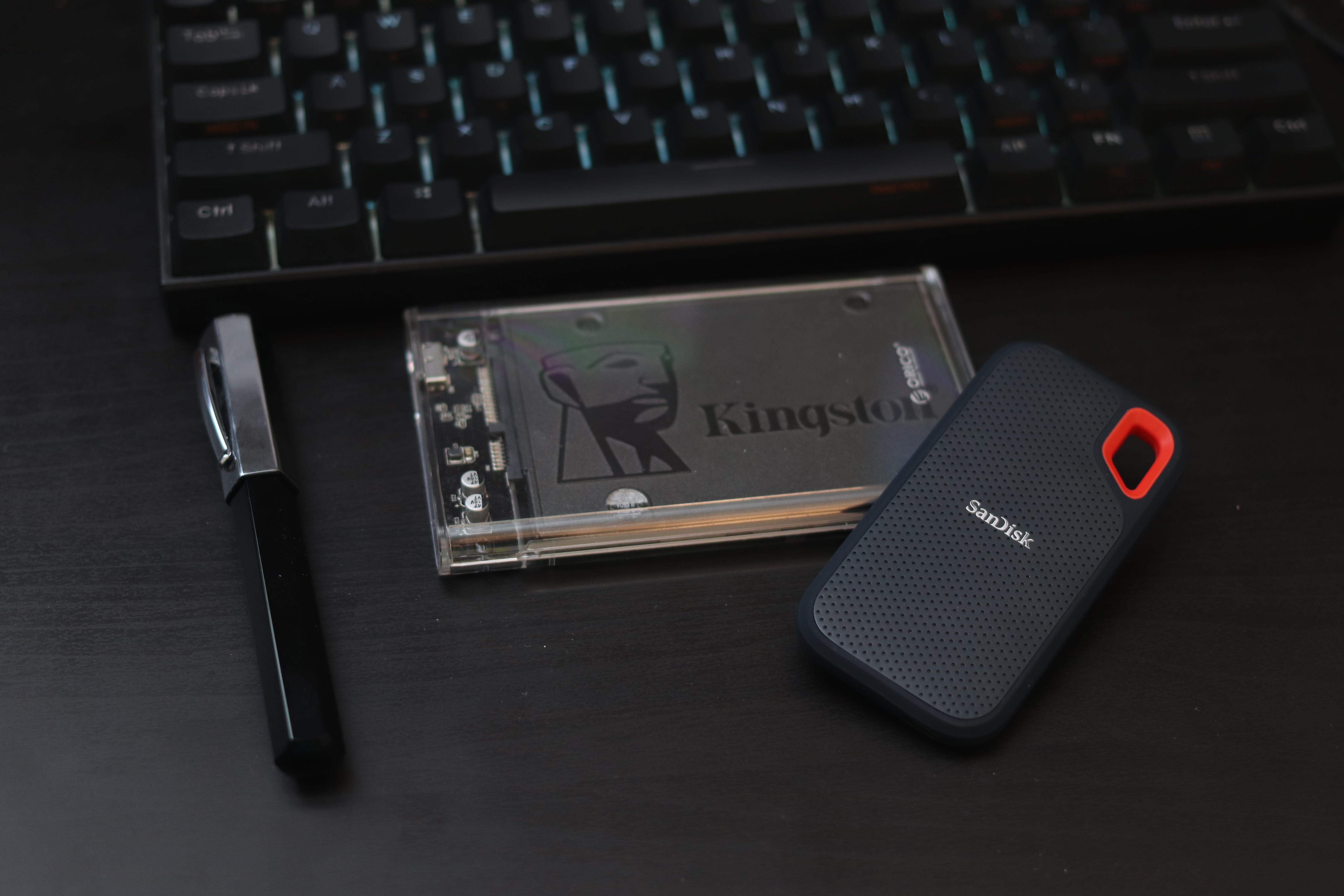 A Kingston SSD drive in a see-through 2.5-inch enclosure, and a smaller Sandisk SSD laying on top of it.