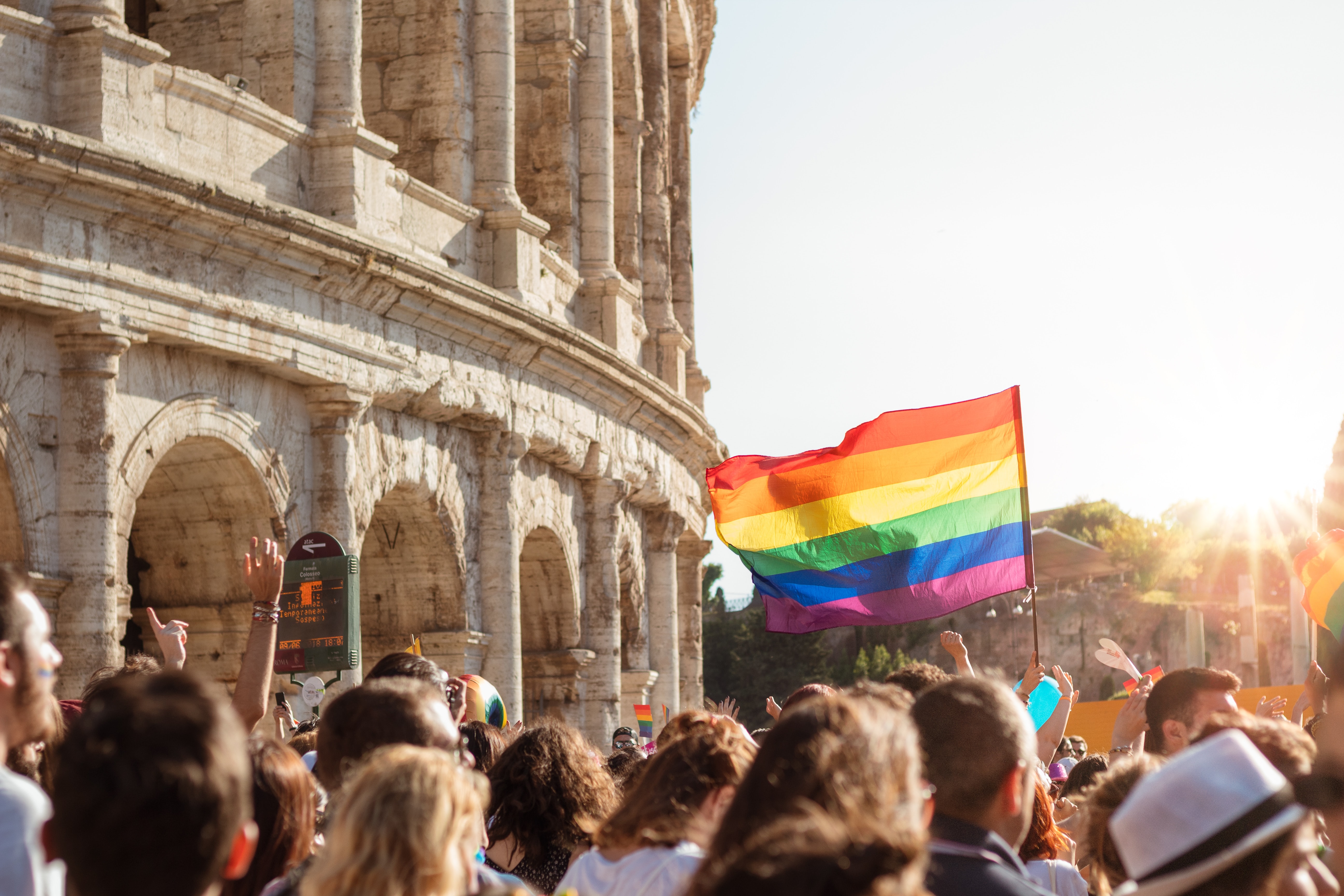 Rainbow flag raised amongst a crowd next to Colesseum in Rome.