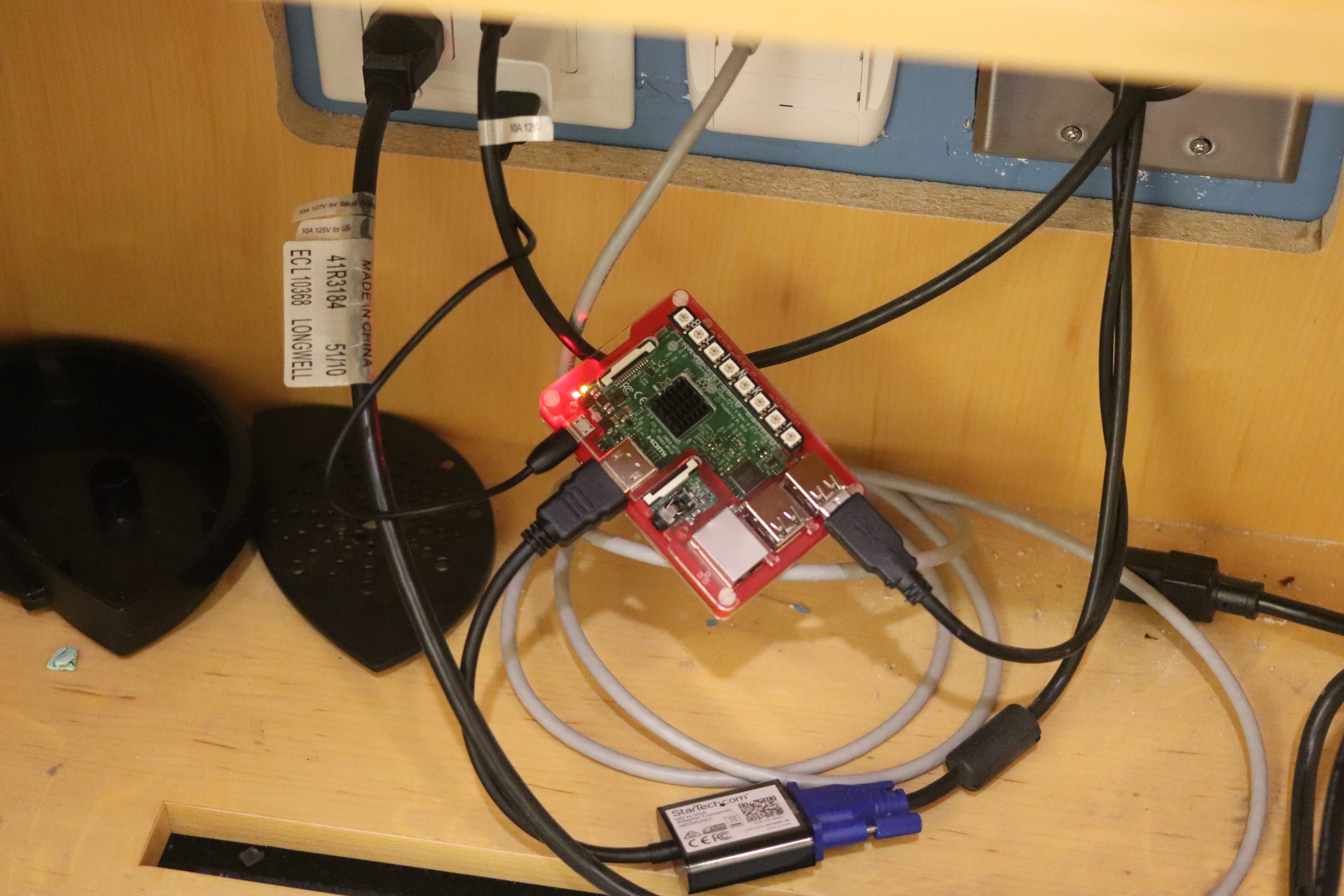 The VGA adapter, power brick, USB cable all plugged into the Raspberry Pi, inside the cabinet, looking messy.