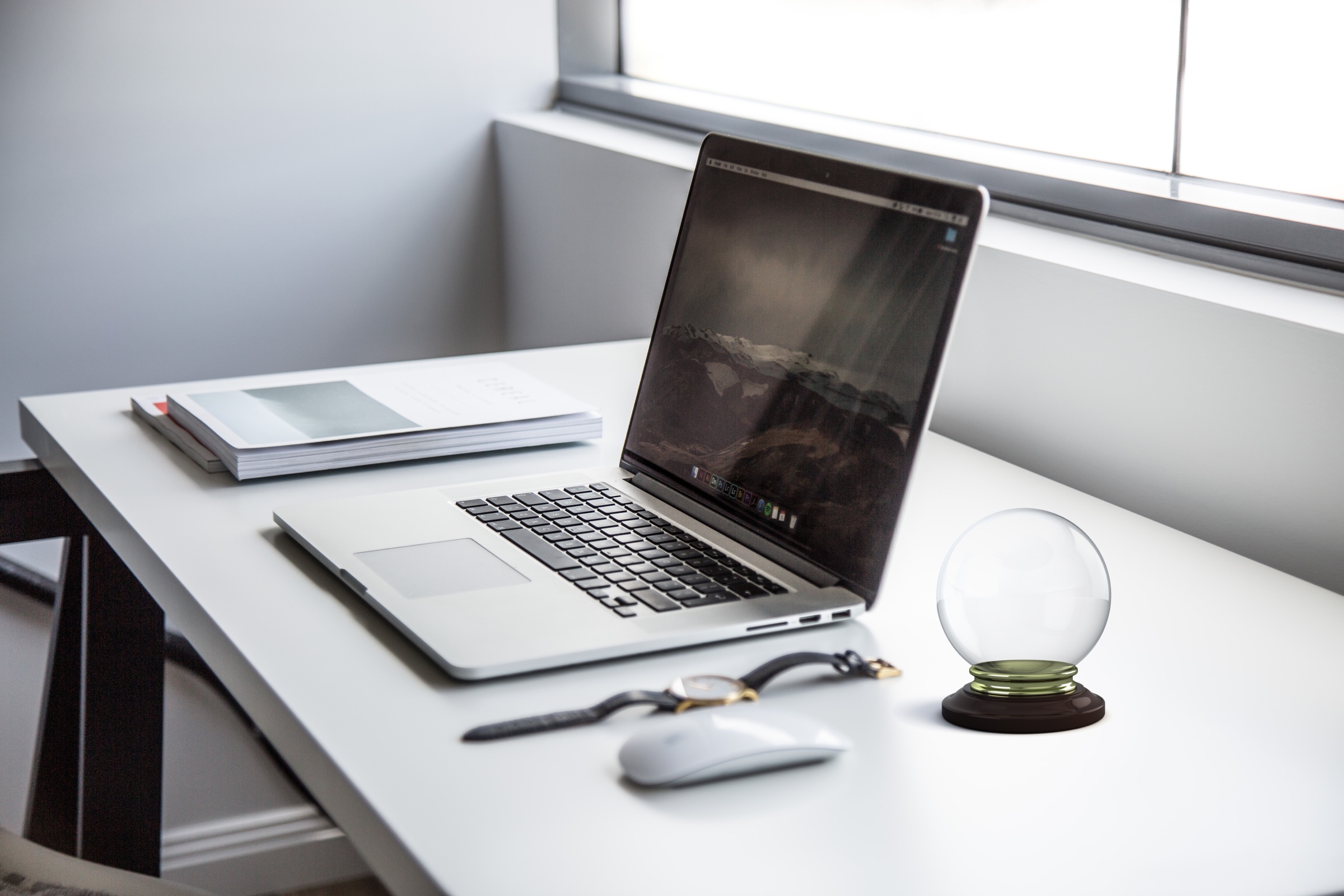 A desk with an open laptop, with a crystall ball next to it.